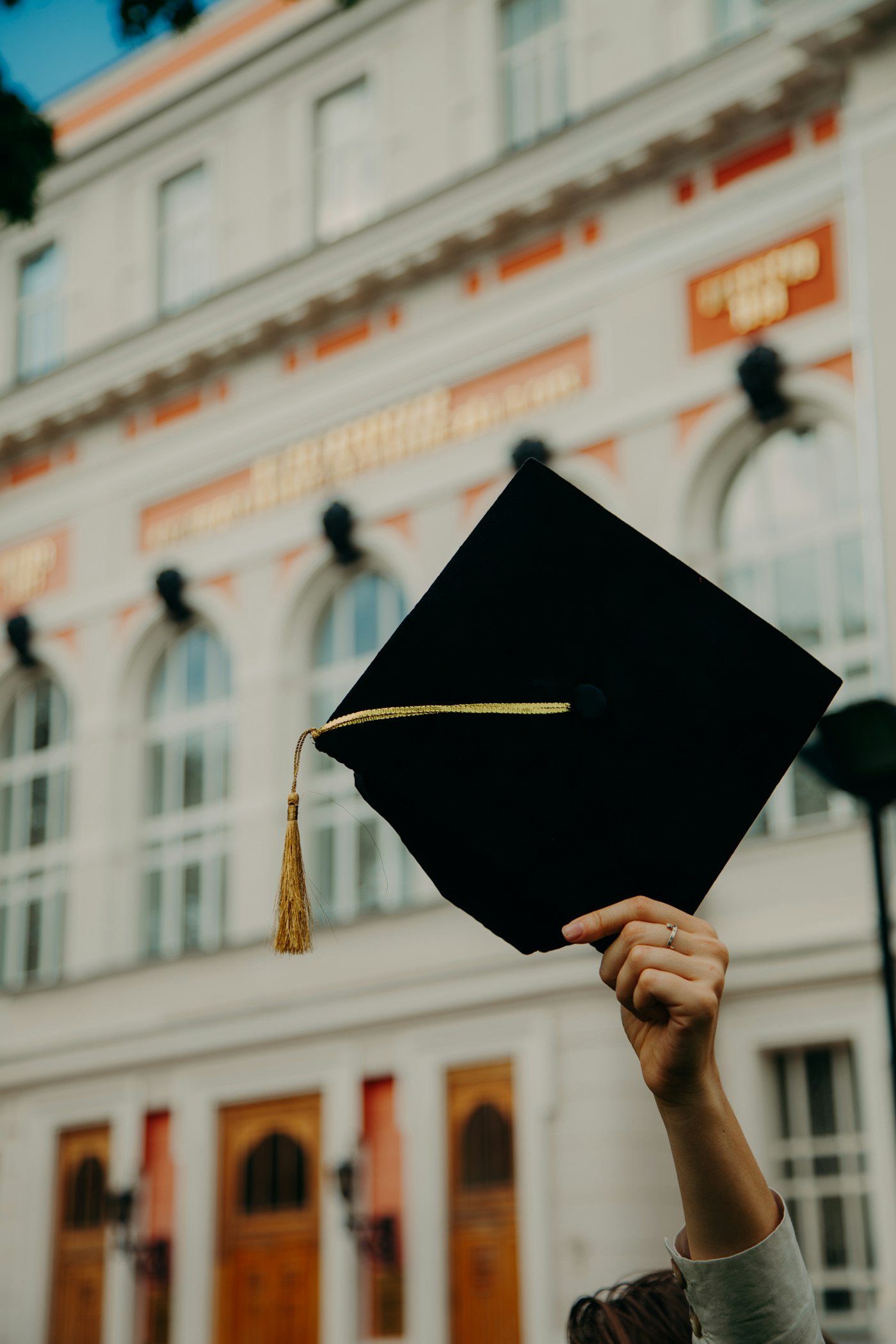 A graduate holding a cap in front of a university building